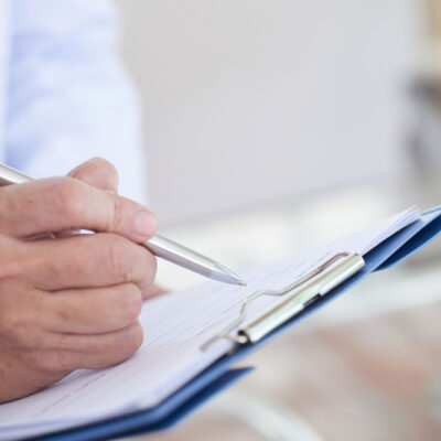 Inspector practicing effective home inspection report writing while holding a pen to paper on a clipboard.