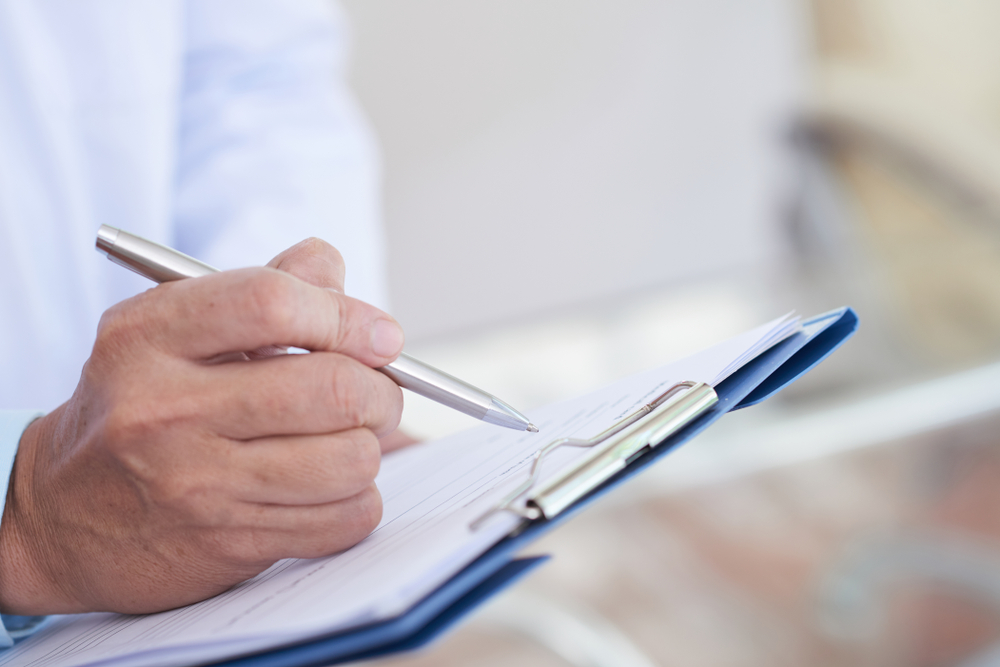 Inspector practicing effective home inspection report writing while holding a pen to paper on a clipboard.