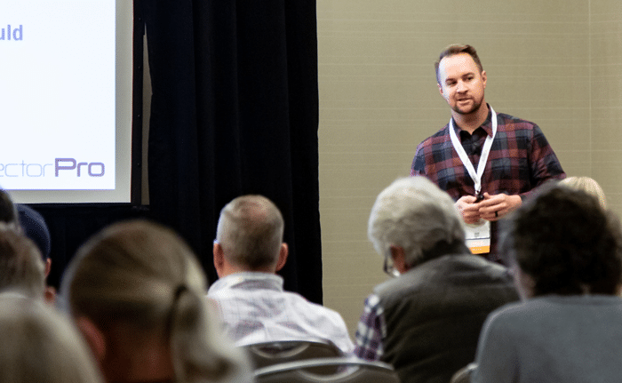 Man (Will Colton) gives a presentation at an American Society of Home Inspectors (ASHI) event in front of a crowd of people.