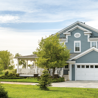 Front of light blue, multi-story home, showing white garage door and porch, as well as large, green, front yard and driveway