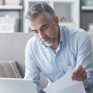 Man with greying hair and beard, wearing a very light blue, collared, long-sleeved shirt and looking through paperwork