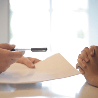 Signatures being taken in a home, with one person handing paper and pen to someone across a table; only hands are visible, not faces