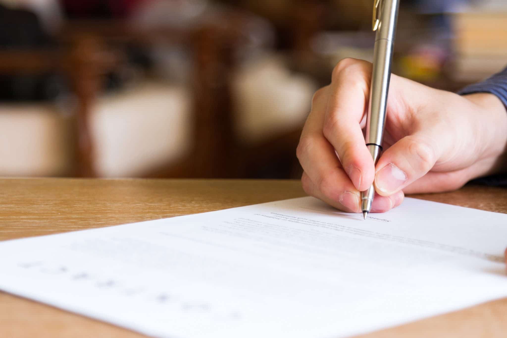 Hand holding pen to sign a printed document, just as a home inspection client must sign an agreement before their inspection