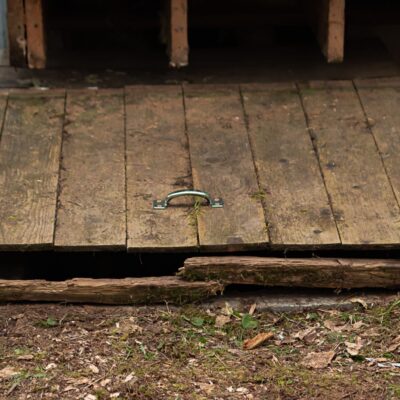 Old, wooden hatch to a small crawlspace, showing signs of age and crawlspace safety concerns.