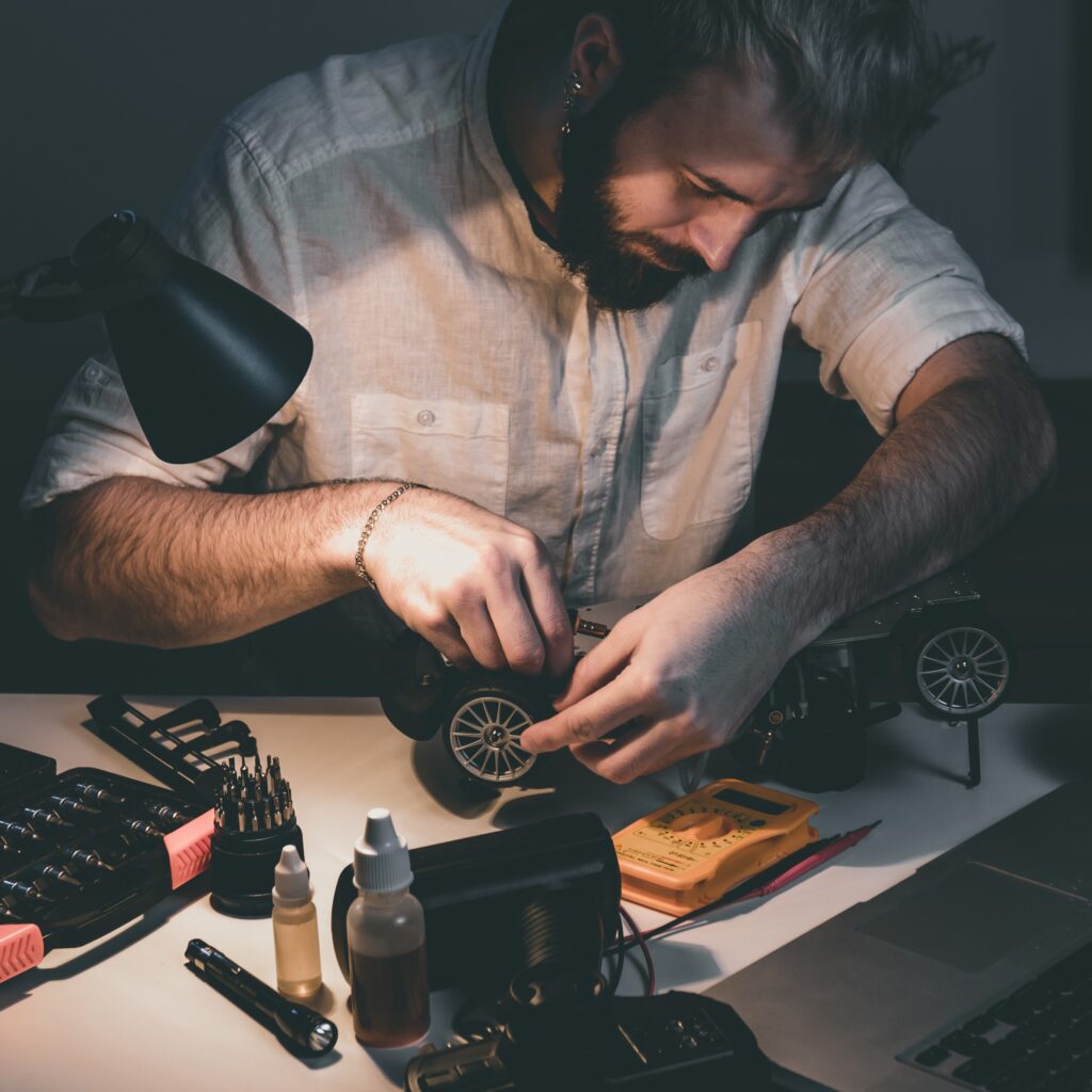 Person building an inspection robot, DIY crawlspace inspection robot, or other similar robotics project with tools and lights on the table.