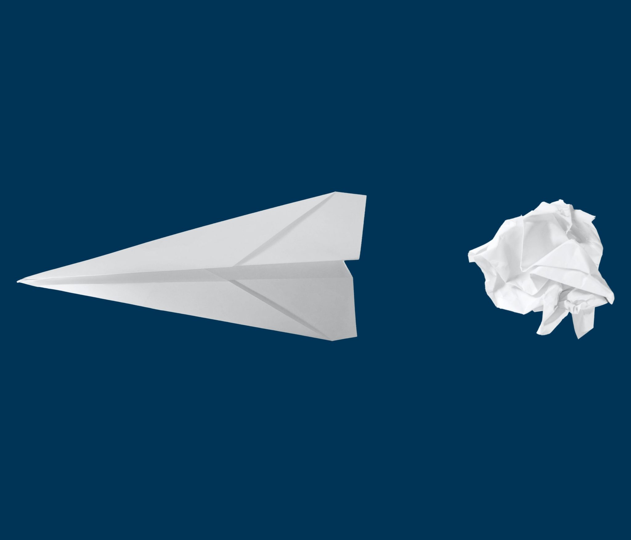 Arrow made of paper airplane and crumpled ball of paper against a dark blue background