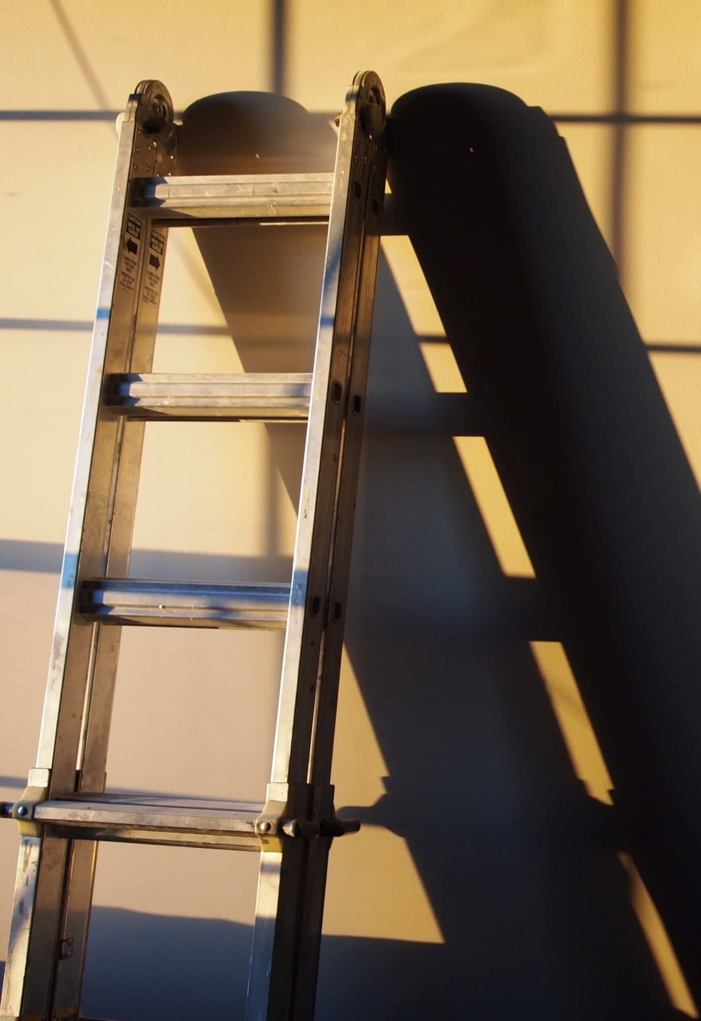 Aluminum ladder leaning against yellow wall, illustrating a common ladder for home inspectors