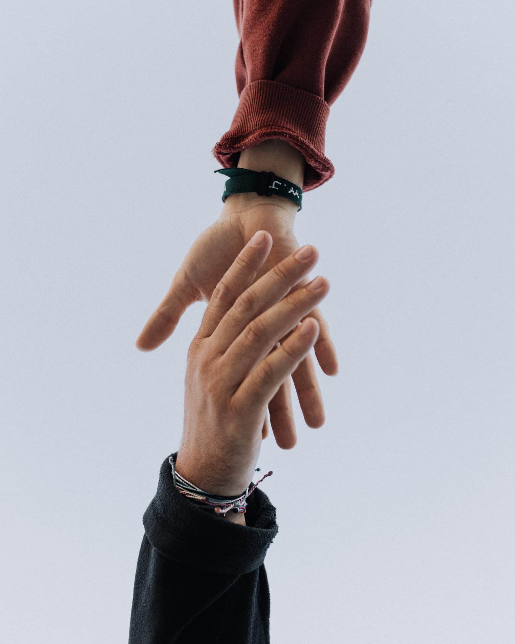 Close-up view of two people's hands reaching out to grasp each other, as if offering their support through anxiety and burnout