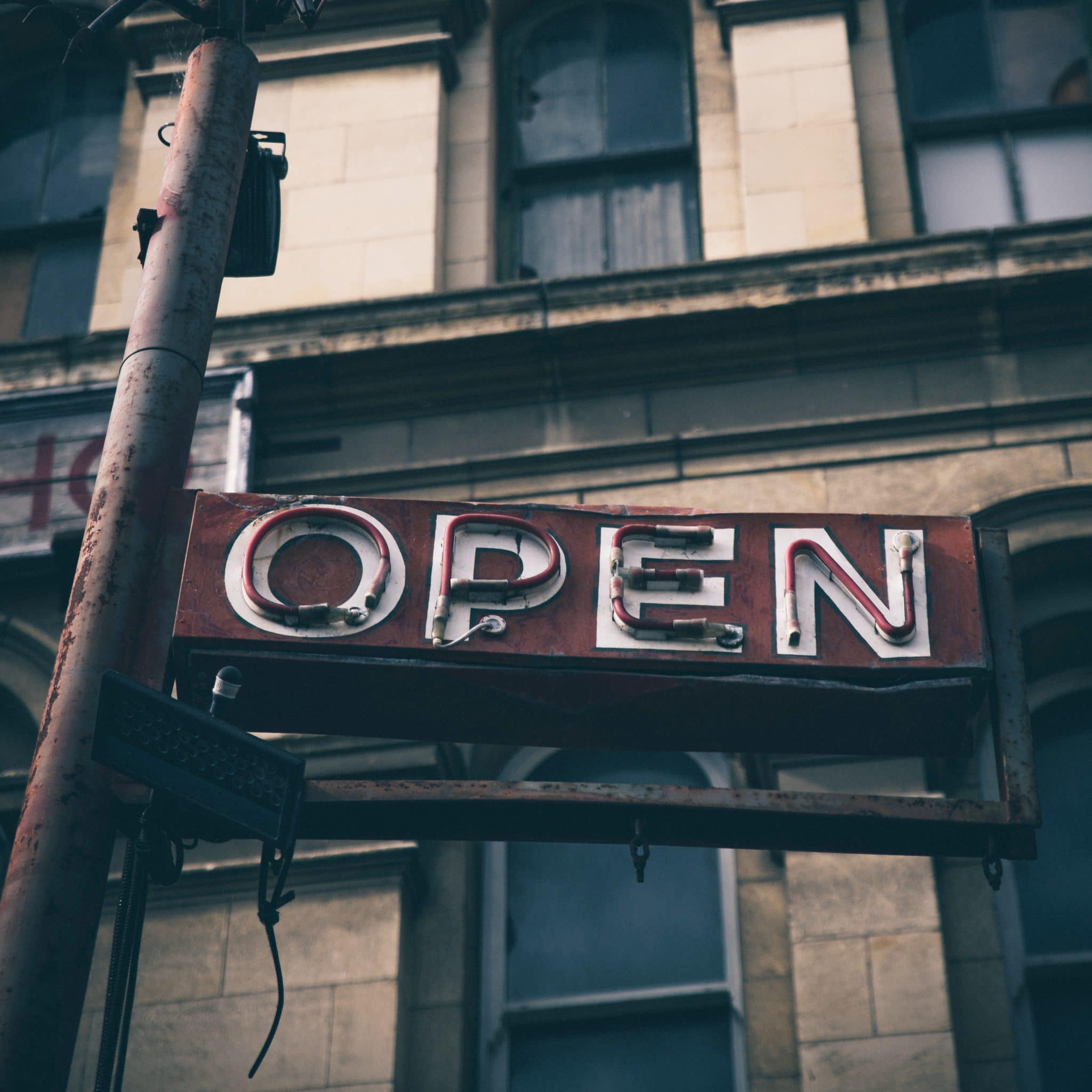 Unlit, neon business "Open" sign on city street