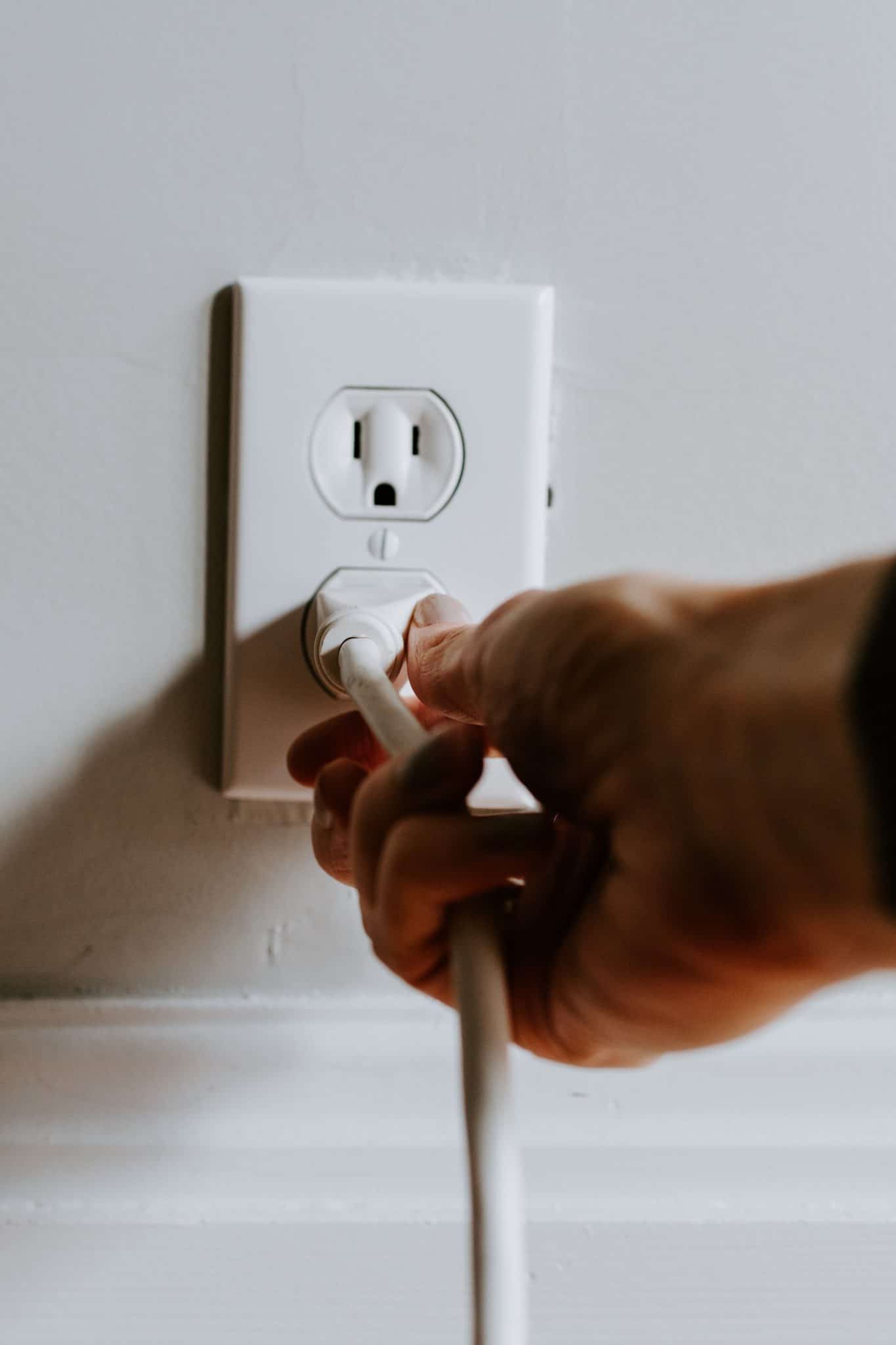 Hand of person unplugging an electrical chord from an outlet