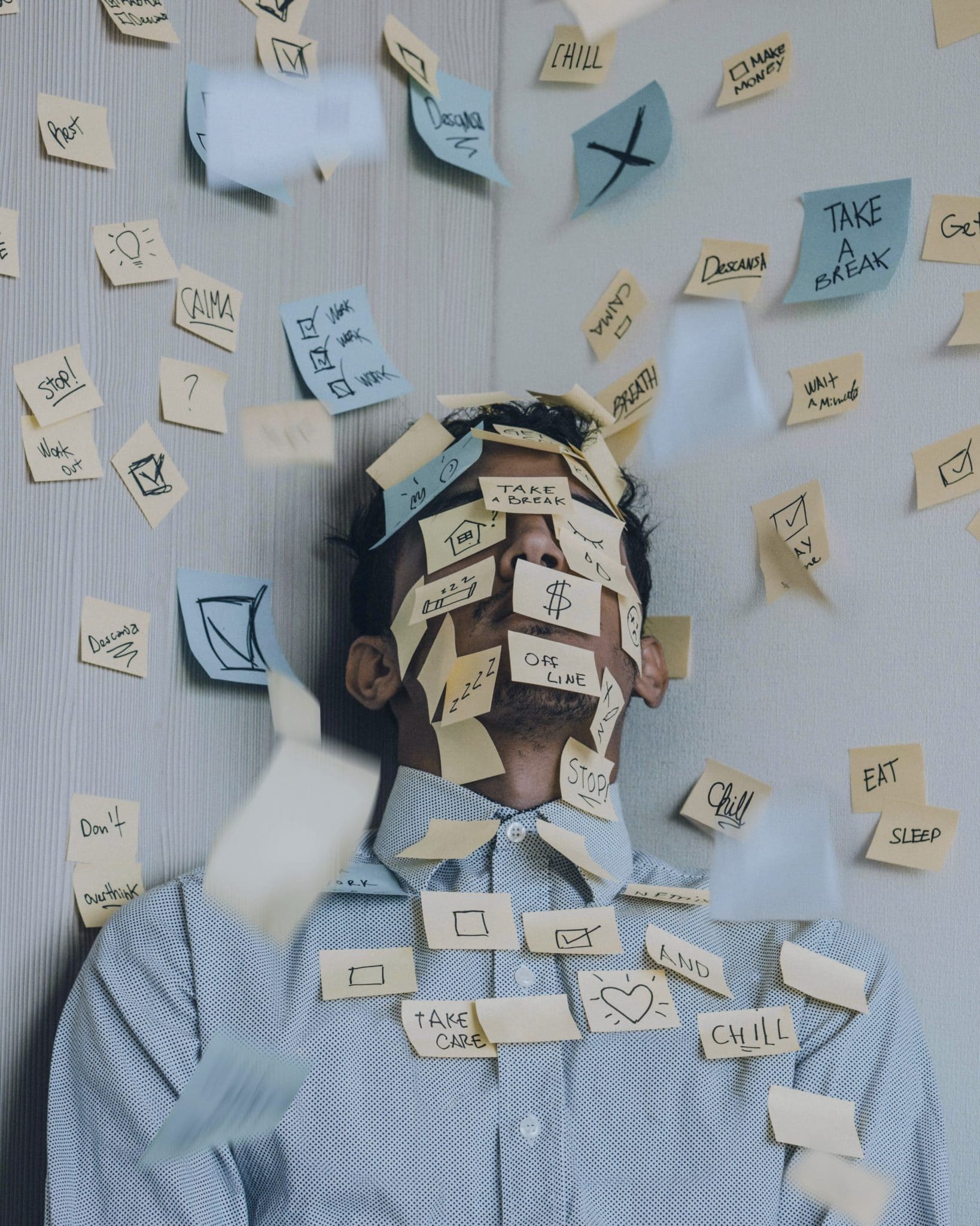 Man with anxiety and burnout leaning against wall, with countless sticky notes covering his face, shirt, and background