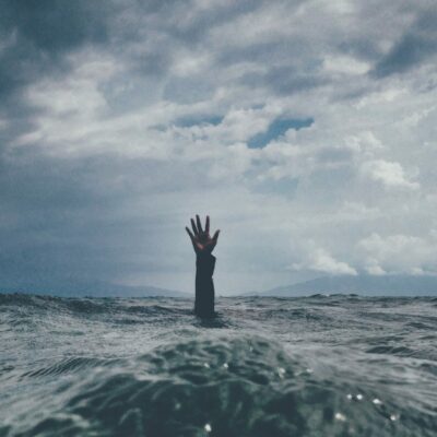 Rough, stormy, grey ocean with arm of drowning person reaching through surface for help.