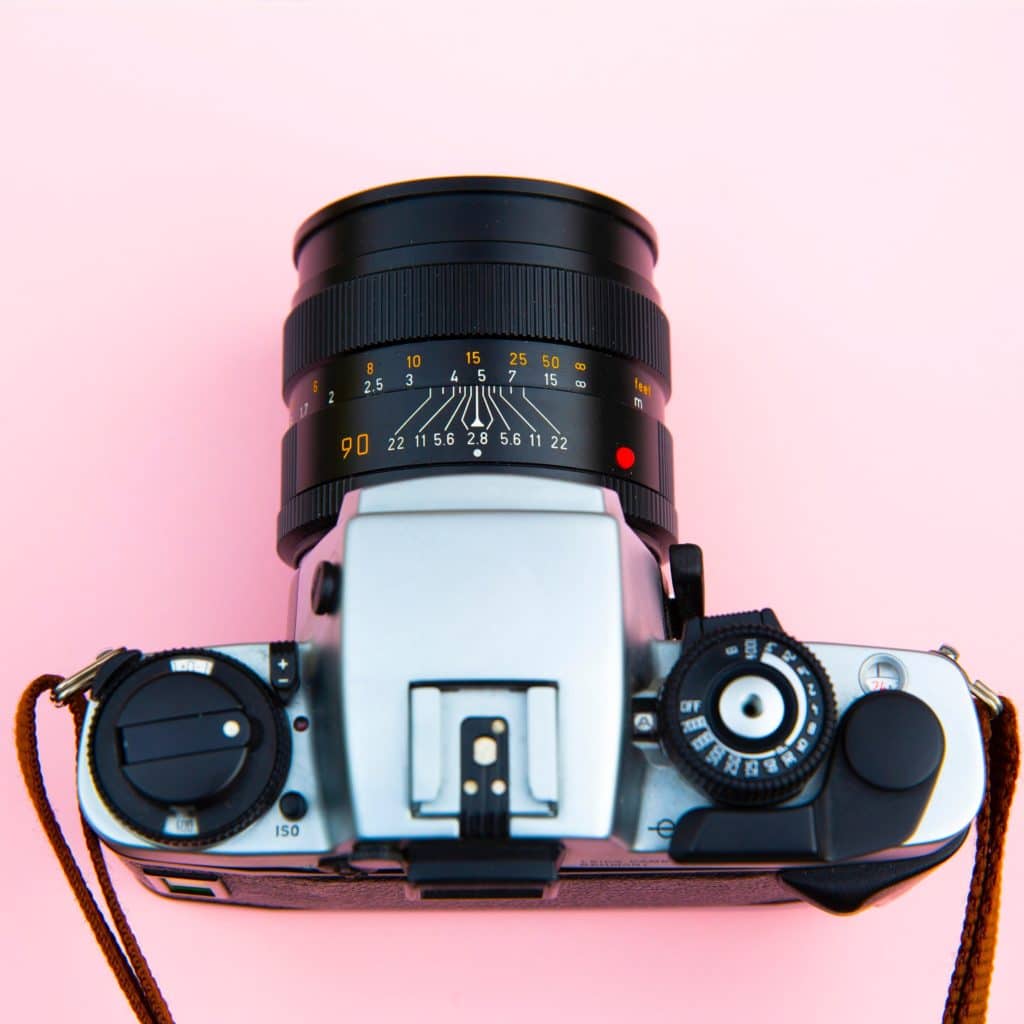 Old-fashioned camera with zoom lens and straps, on top of a pink surface