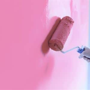 Zoomed in to show a man's hand, using a roller to paint a wall pink