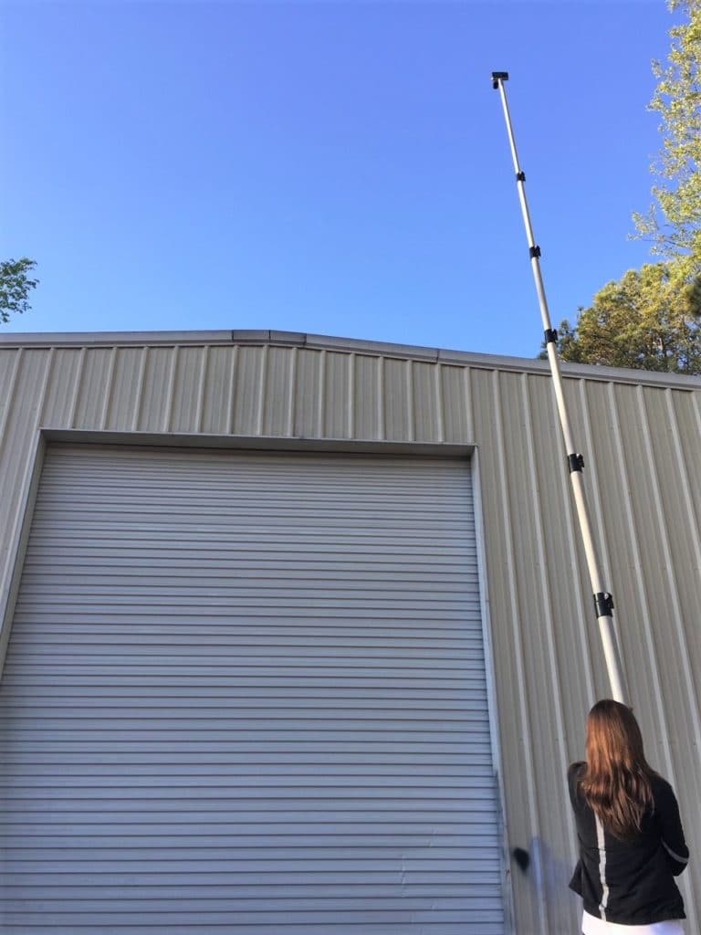 Inspector holding extended pole cam above roof of tall, garage-like structure