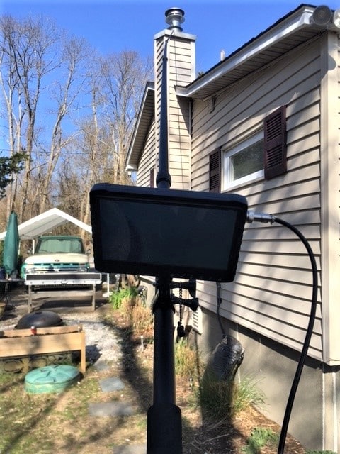 Close-up view of black pole cam monitor, with pole cam extended above home's roof in the background