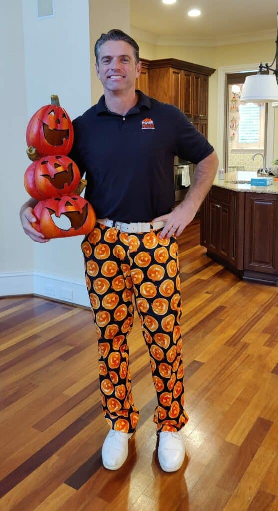 Preston Sandlin, wearing a navy blue HIC shirt, white shoes, and jack-o-lantern pants, holding decorative jack-o-lanterns for Halloween.