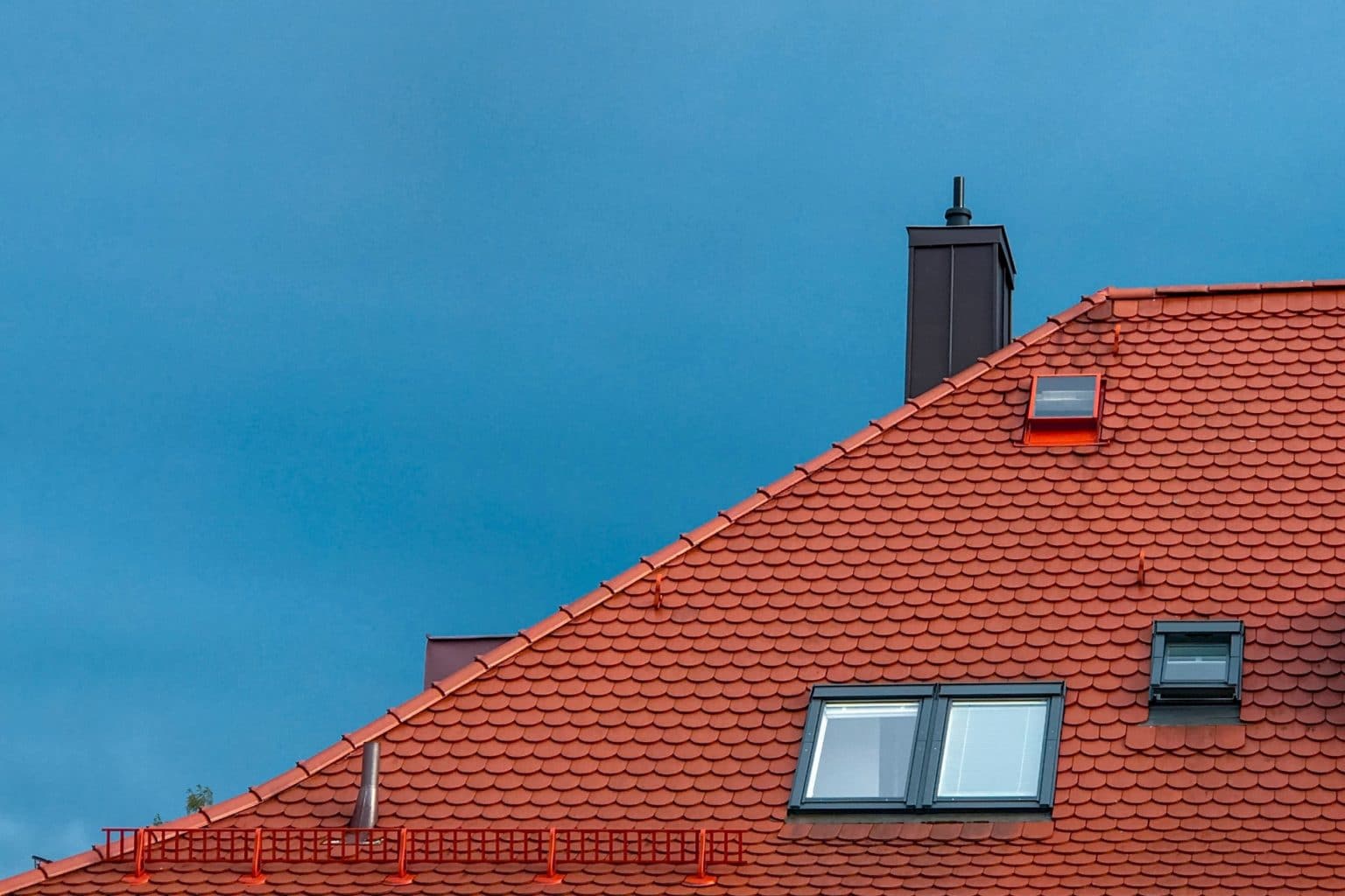 Tall, steep, red roof against a blue sky, communicating a situation that may call for a pole cam