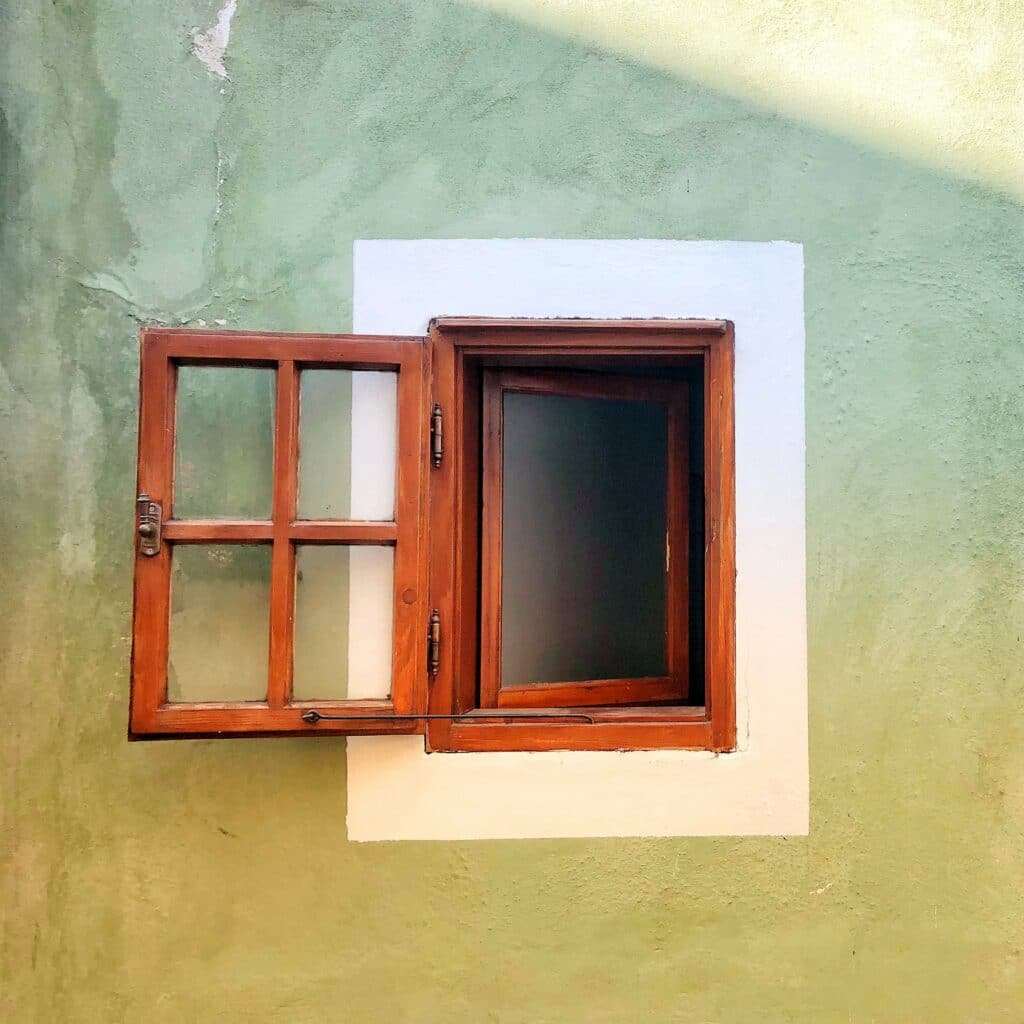 Reddish-brown, wooden, rectangular window, small, opened out with a backdrop of a wall painted mint and lime green