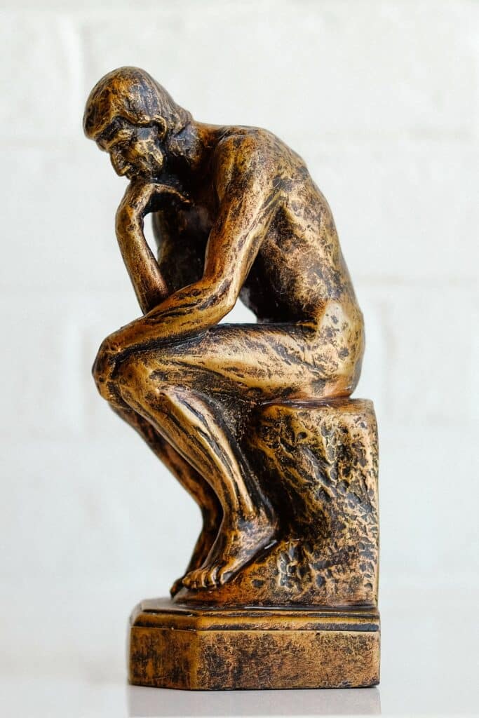 Yellow rendition of The Thinker Statue by Auguste Rodin against white background