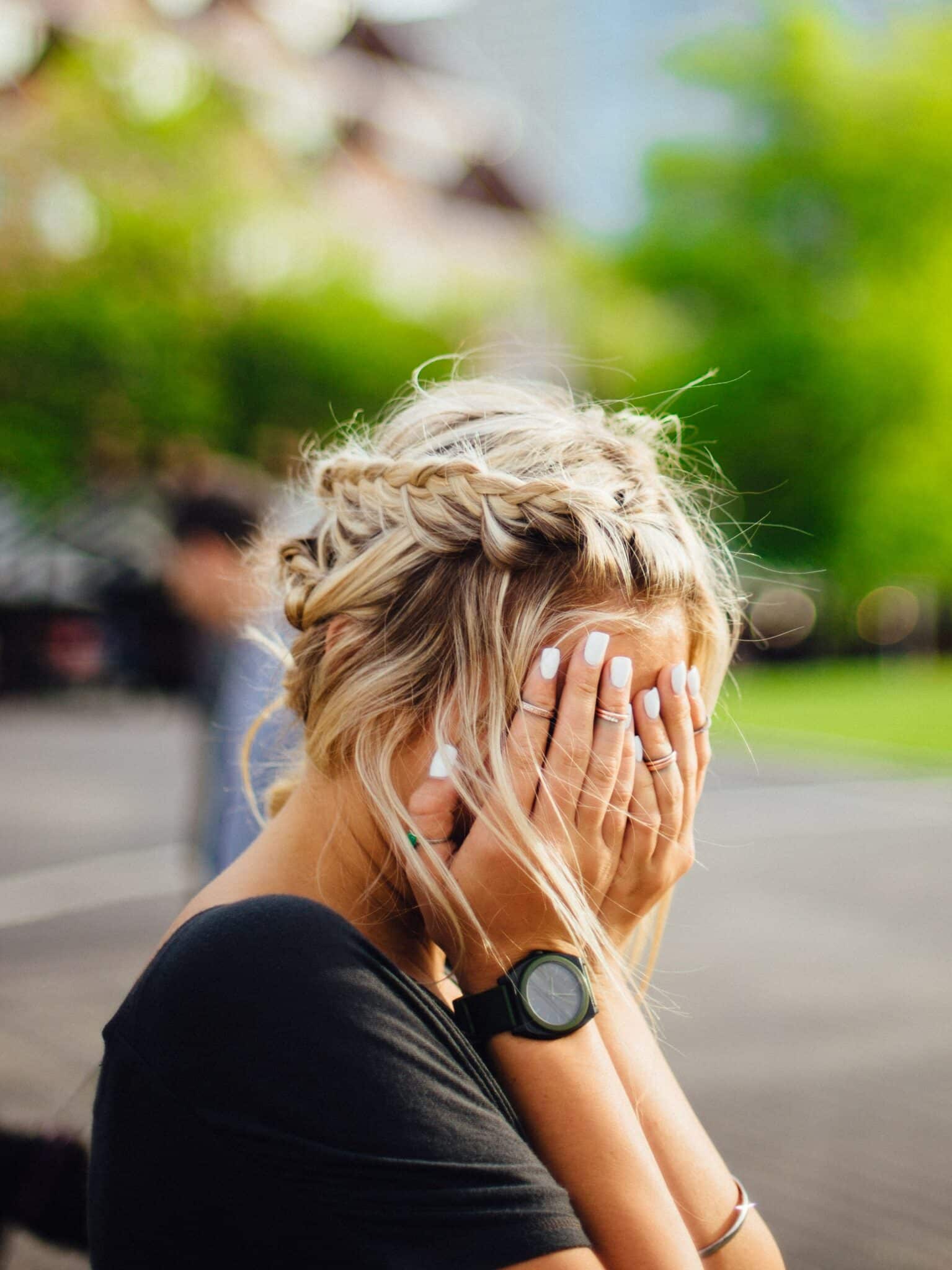 Woman sitting on park bench while covering her face with her hands in a sad or frustrated expression