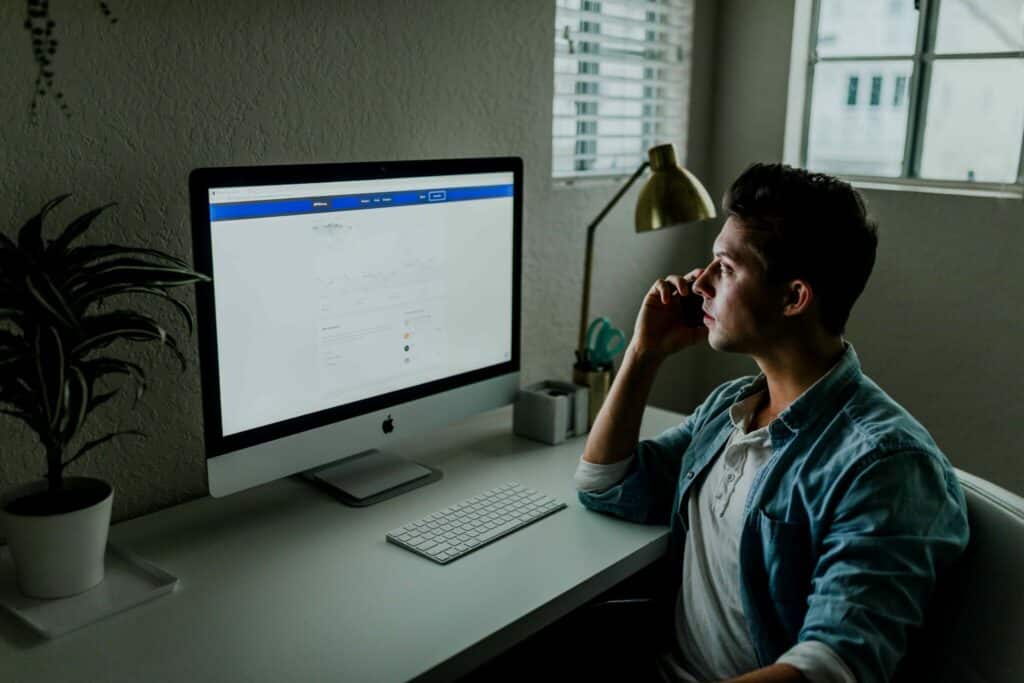 Man sitting at desk, looking at computer screen and presumably using an inspection report writing software while holding a phone to his ear