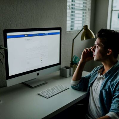 Man sitting at desk, looking at computer screen and presumably using an inspection report writing software while holding a phone to his ear