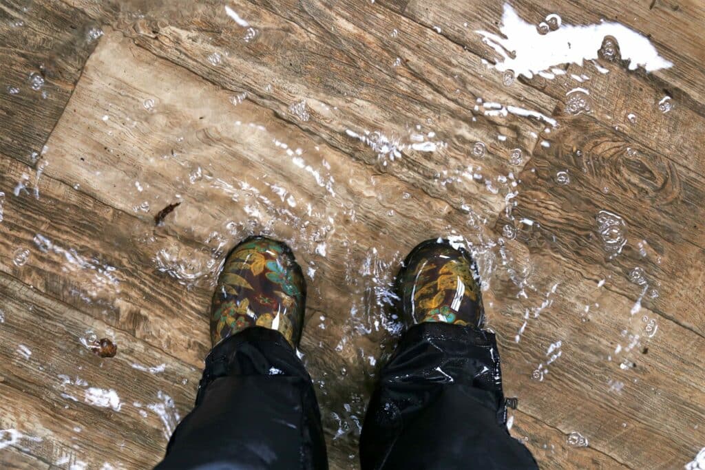 Boots and lower pantlegs of person standing in water, presumably in a room flooded by an issue like a burst water pressure pipe (like in this claim)