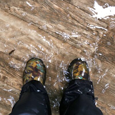 Boots and lower pantlegs of person standing in water, presumably in a room flooded by an issue like a burst water pressure pipe (like in this claim)