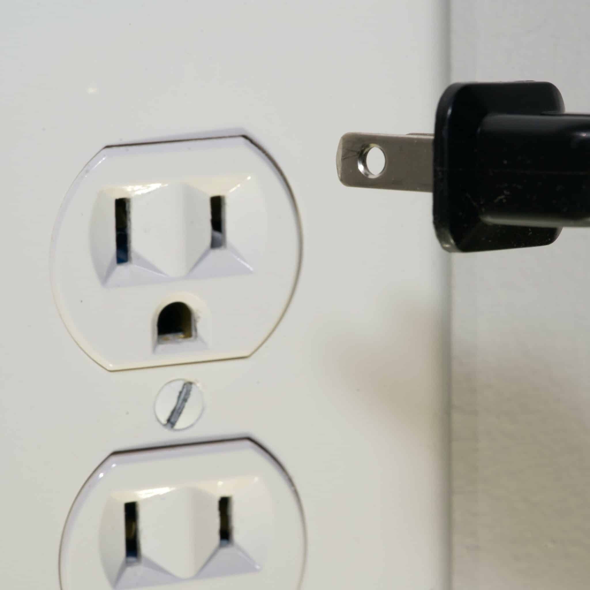 White electrical outlet with electrical plug approaching