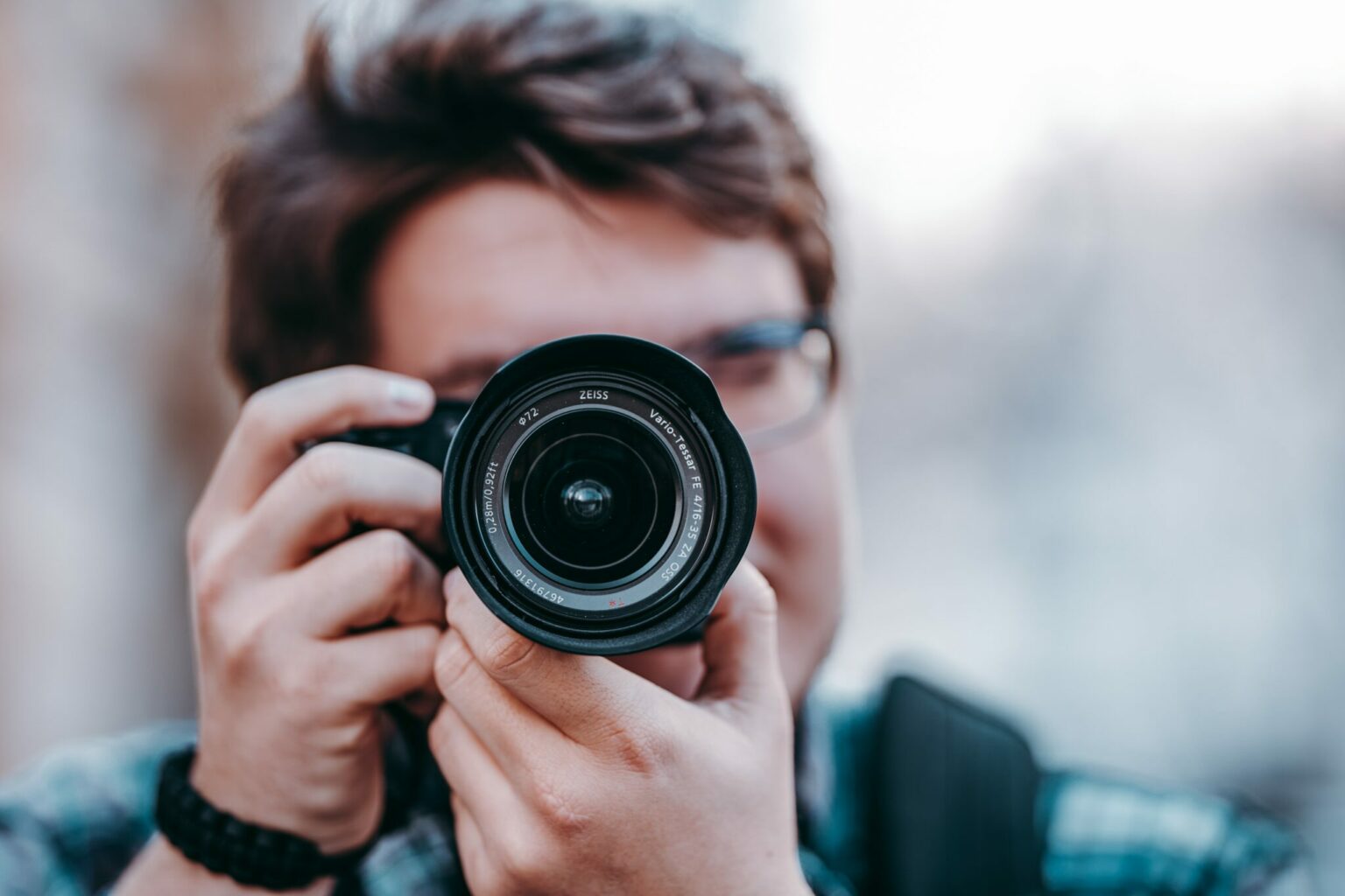 Person with short hair and glasses holding camera up to face