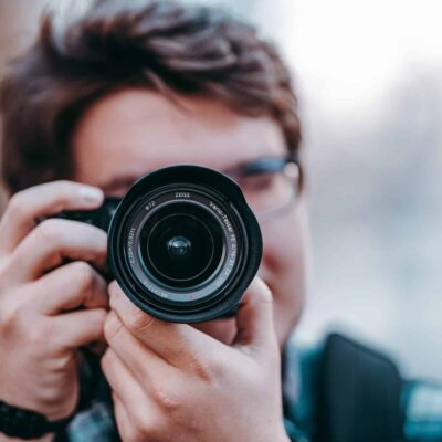 Person with short hair and glasses holding camera up to face