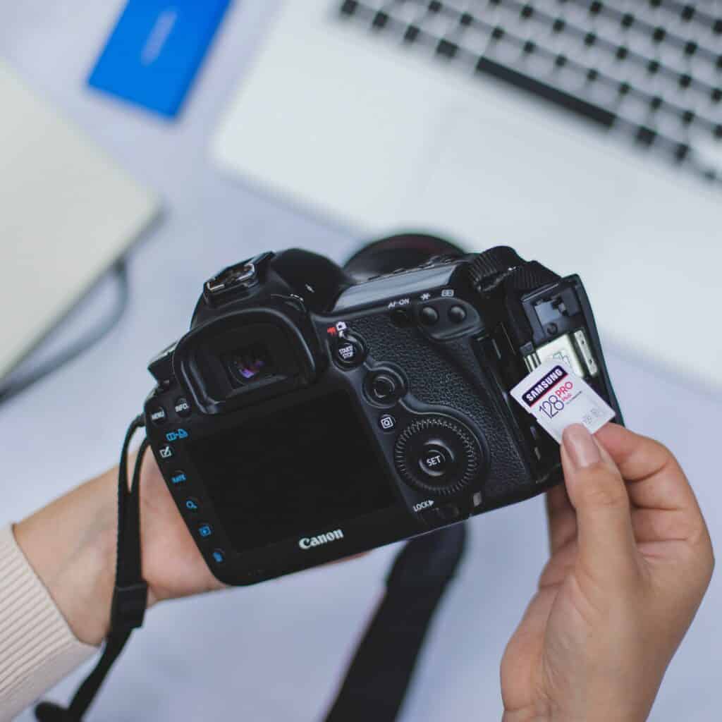 Close up of Canon camera held up against a Samsung memory card, with a laptop blurred in the background