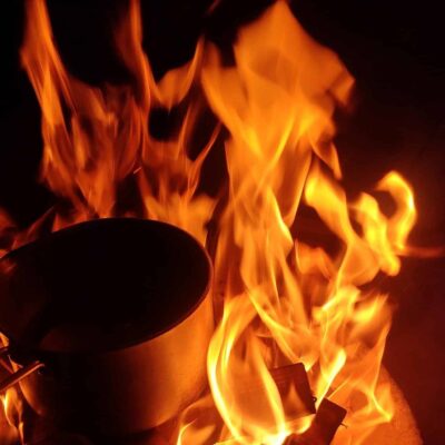 Metal cooking pot placed in a large, bright fire at nighttime