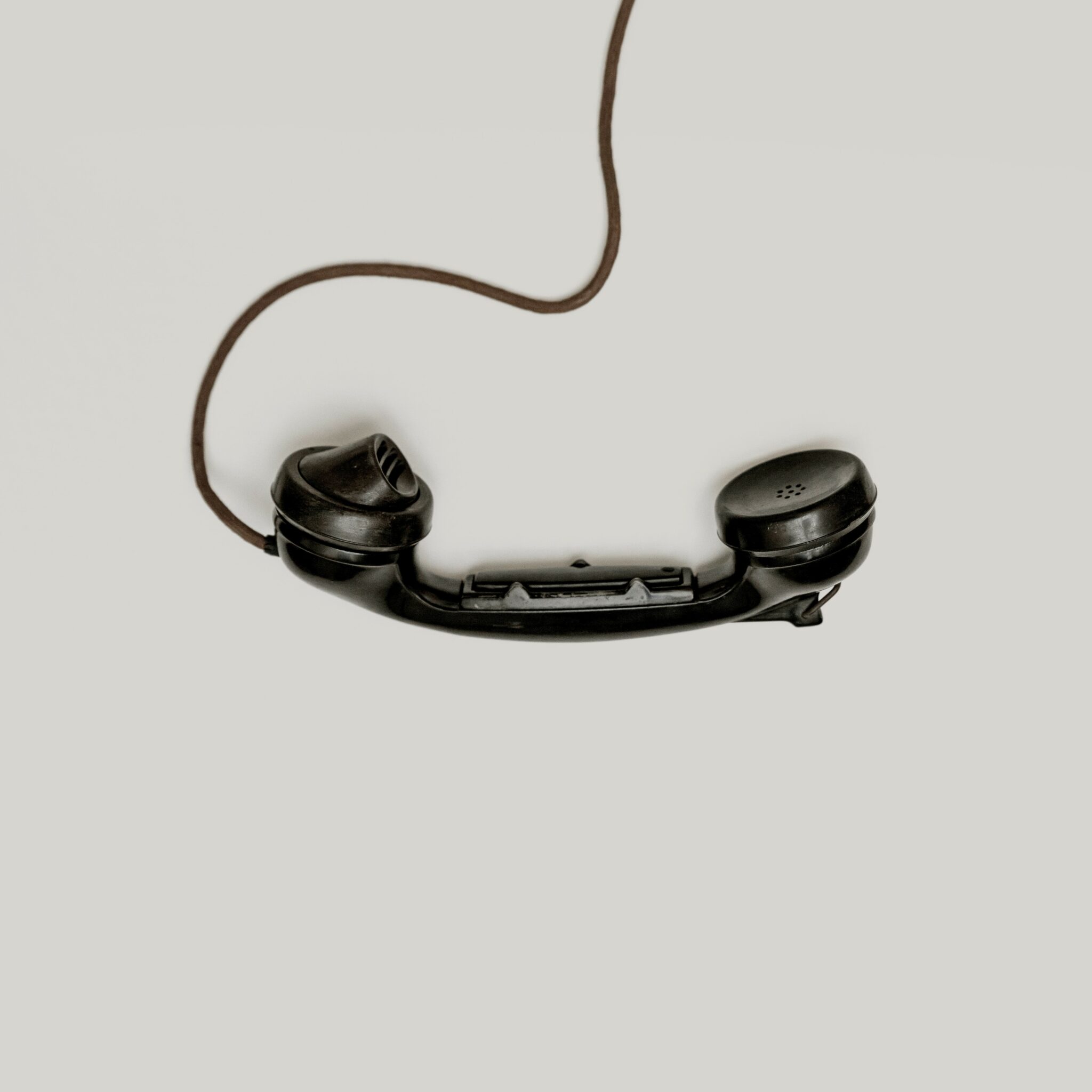 Black, old fashioned phone dangling by a chord on a grey background.