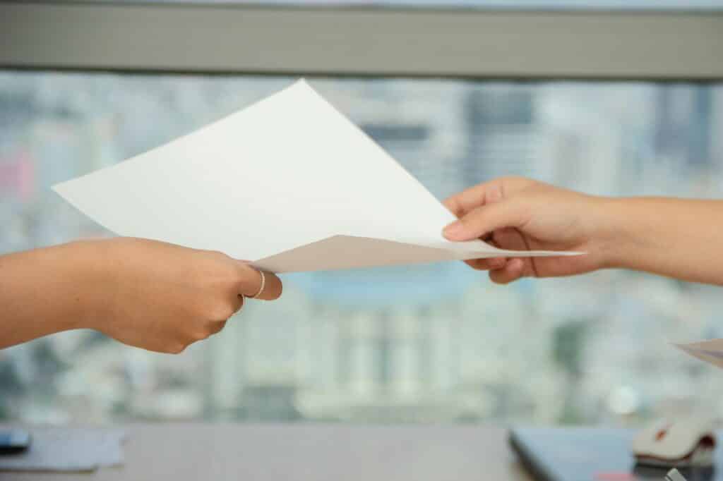Zoomed in view of two feminine, Caucasian hands passing a blank, white sheet of paper from one to the other, presumably between two women. Used to illustrate release of claims or release of liability contract as a means of limiting home inspector liability.