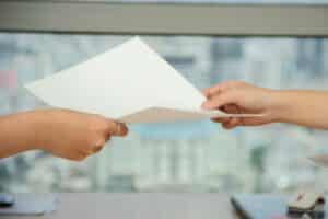 Zoomed in view of two feminine, Caucasian hands passing a blank, white sheet of paper from one to the other, presumably between two women. Used to illustrate release of claims or release of liability contract as a means of limiting home inspector liability.