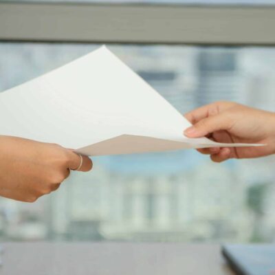 Zoomed in view of two feminine, Caucasian hands passing a blank, white sheet of paper from one to the other, presumably between two women. Used to illustrate release of claims or release of liability contract as a means of limiting home inspector liability.