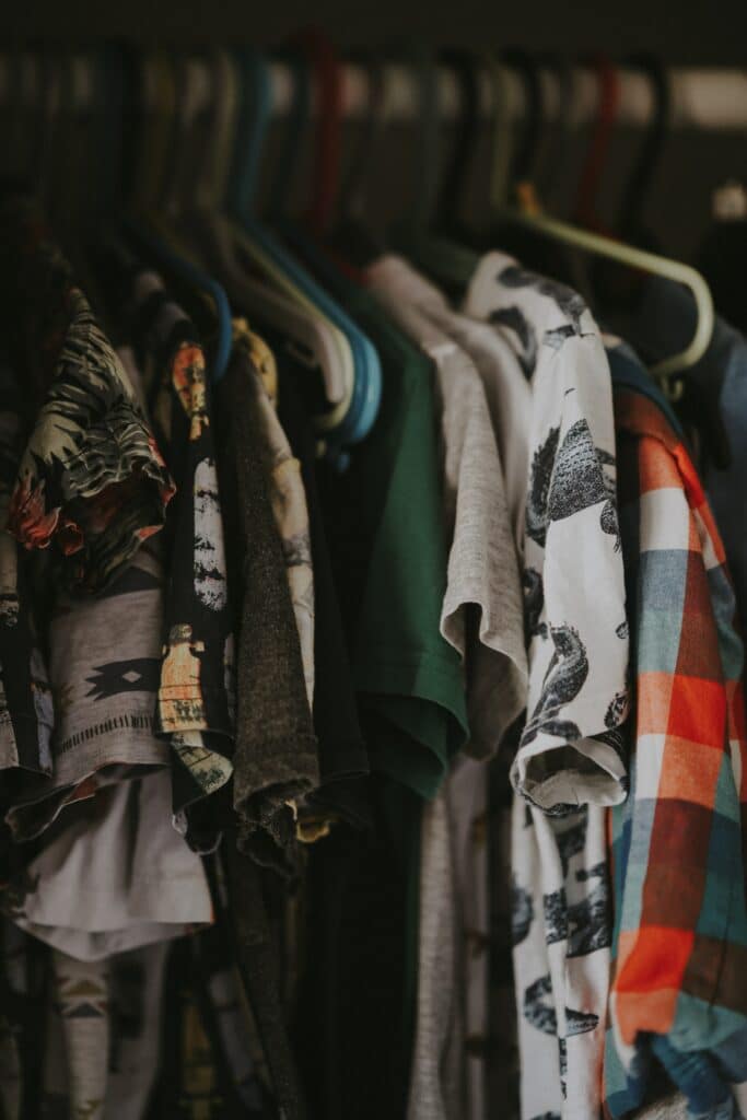 Dark closet packed tightly with collared, colorful, short-sleeved shirts hanging up.