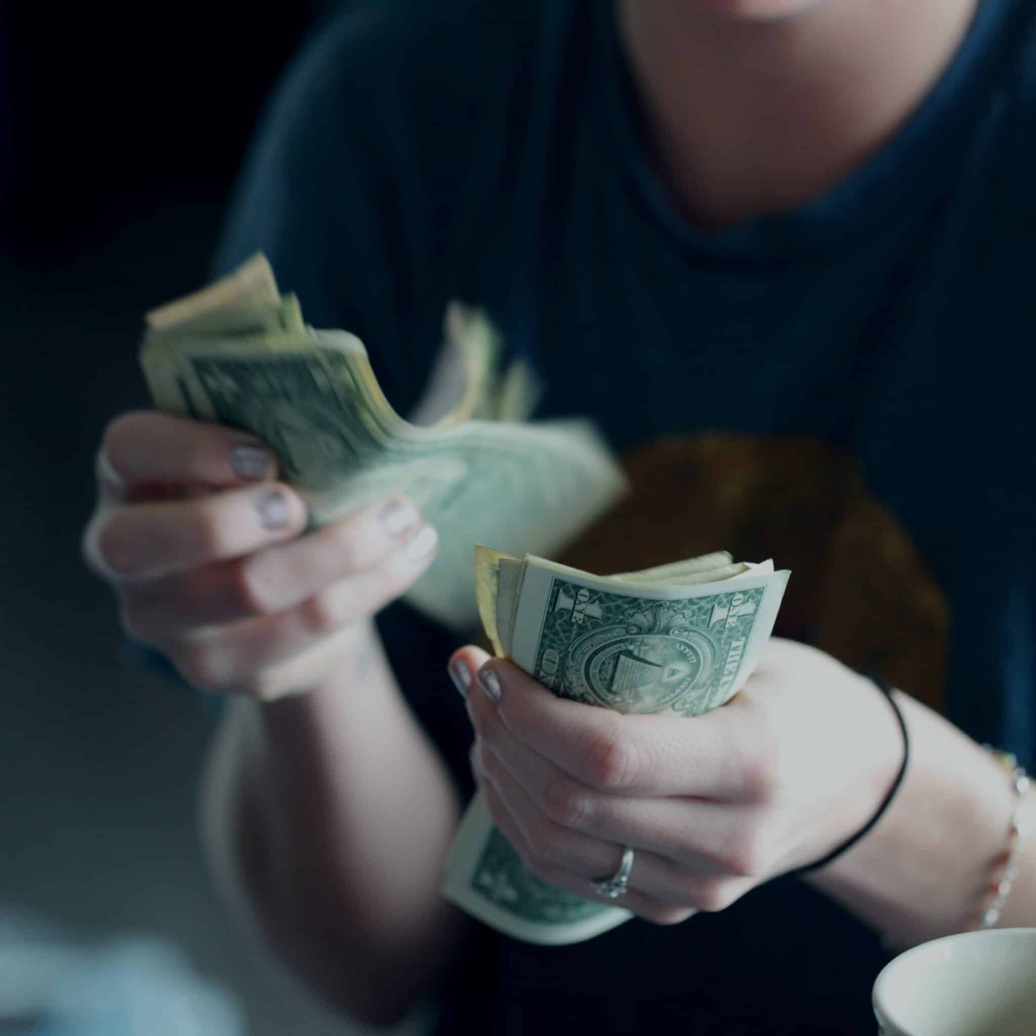 Close-up view of person's hands while counting American dollar bills. Person is wearing a dark shirt and face is out of view.