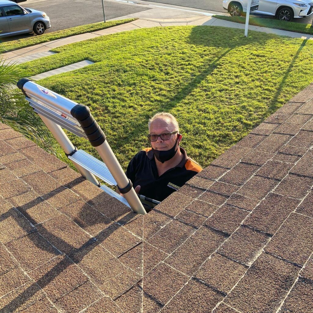 Man wearing glasses looks at camera while climbing a ladder to a roof.