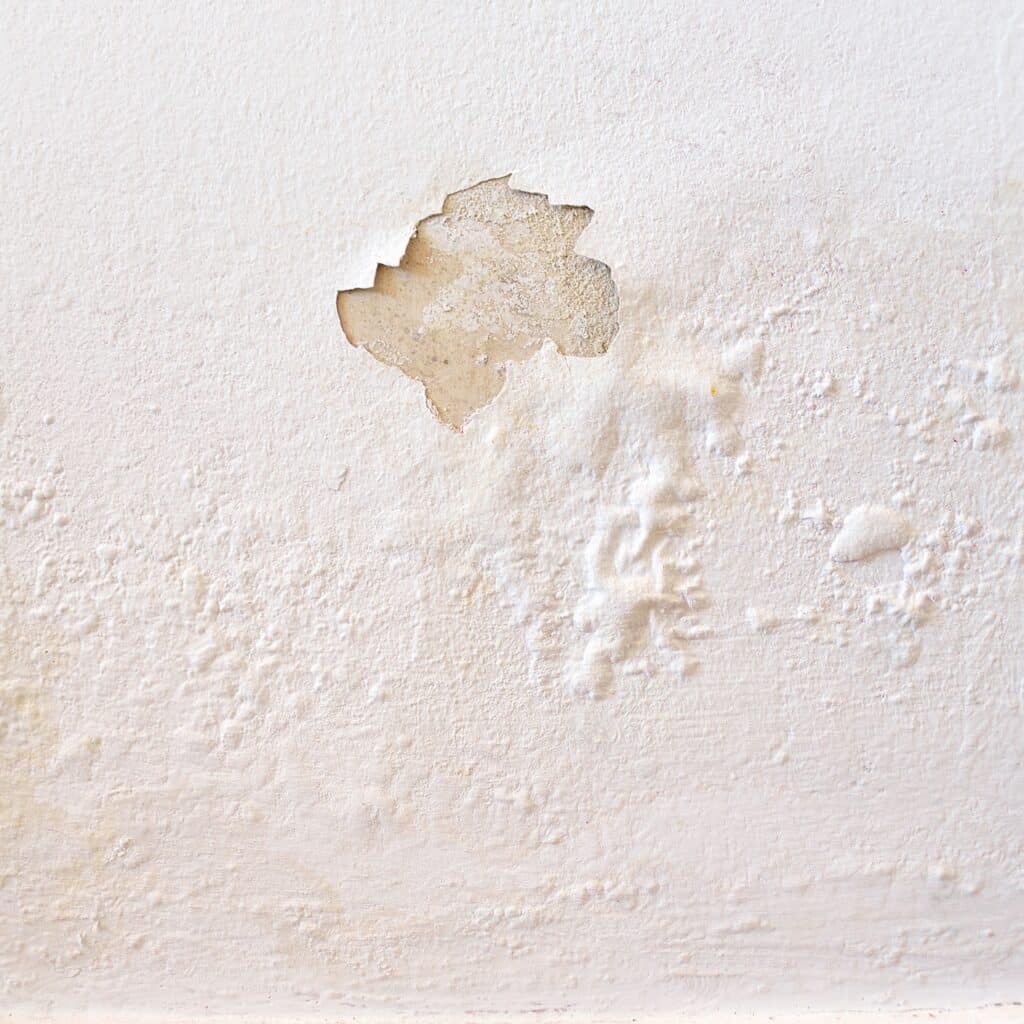 White wall with paint bubbling and peeling due to a water leak, much like the property in this water damage claim.