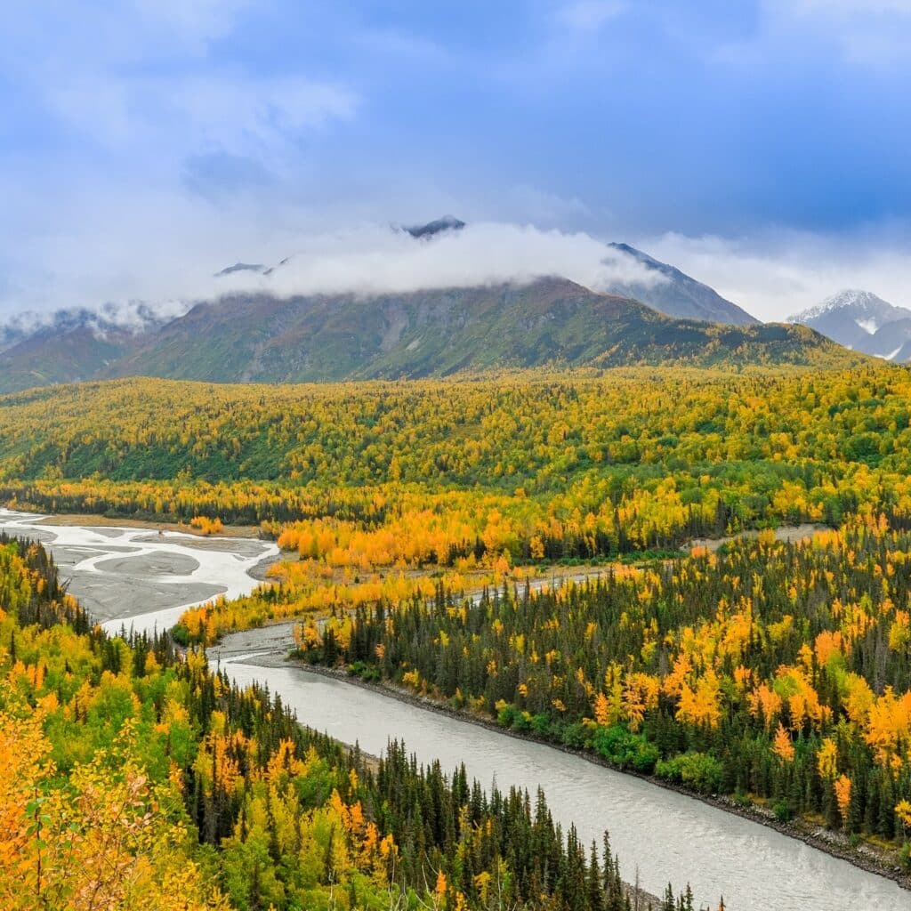 River winding through autumnal trees in Anchorage, Alaska below several mountains, drawing in those learning how to become a home inspector in Alaska.
