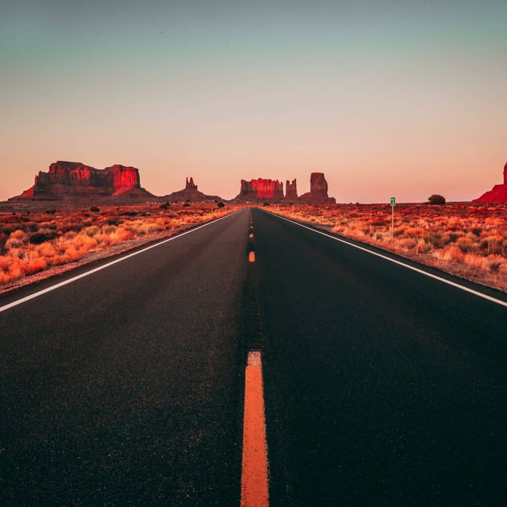 Arizona desert at sunrise or sunset, with rock formations in the horizon along a vast highway