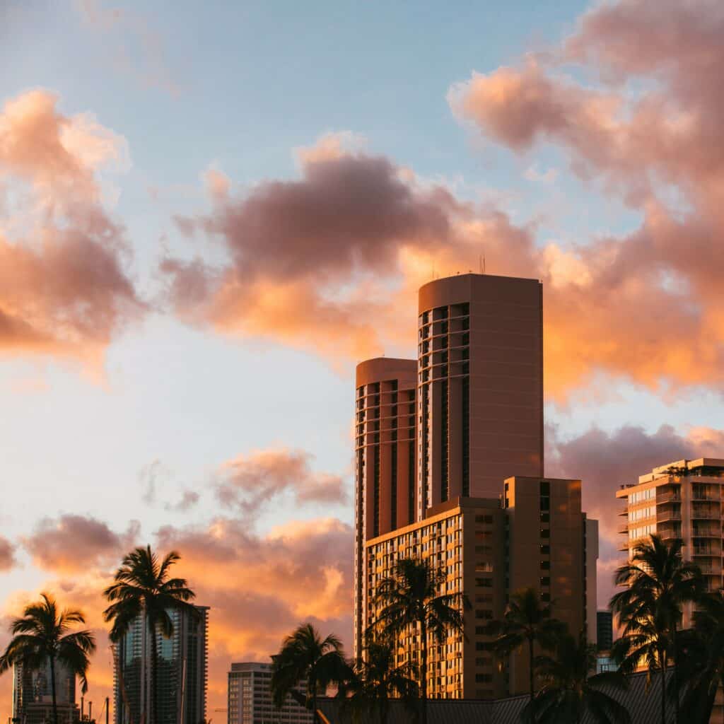 A sunset or sunrise view of skyscrapers and palm trees in Oahu, Hawaii.