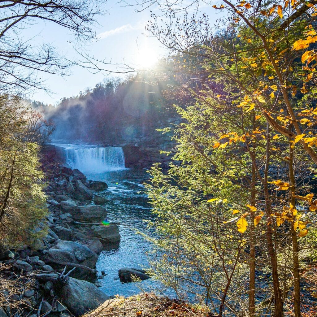 Waterfalls of Cumberland Falls, Kentucky leading to a river, view partially obscured by trees with fall foliage.