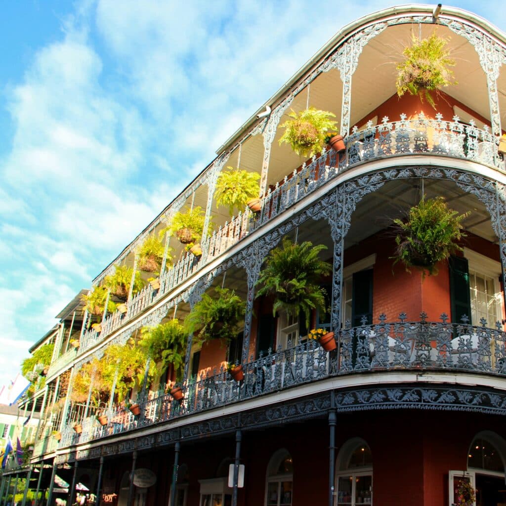 New Orleans, Louisiana view of three-story building with balconies on each level, lined with white, ornate fencing and hanging tropical plants.