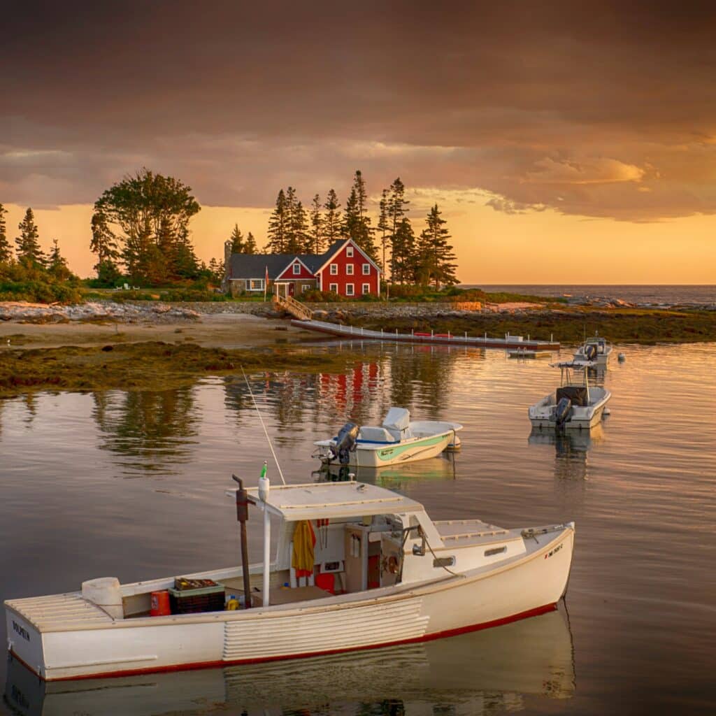 Sunset view of Cape Newagen, Southport, Maine, a red home in the distance at sunset with multiple fishing boats closer to the camera’s eye.
