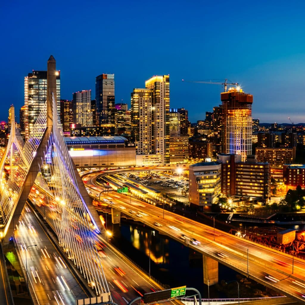 Boston, Massachusetts skyline at dusk above a well-lit freeway bridge.