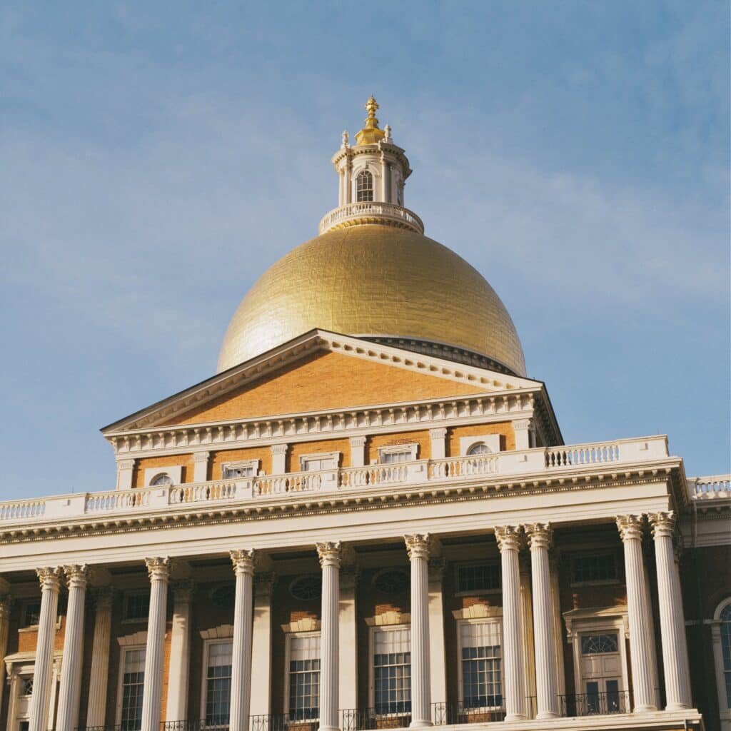 Massachusetts State House at daytime with a golden dome and blue skies.